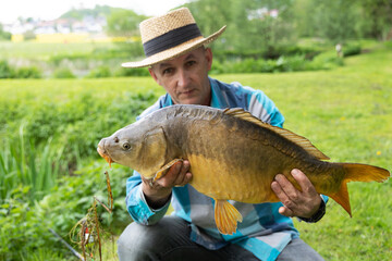 A man is holding a large carp fish caught on a fishing rod