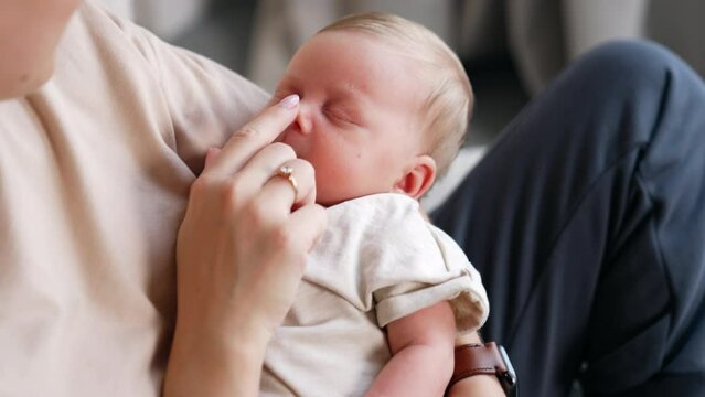 Cropped image of a mom holding her sleeping baby in hands. Mother touches her child's nose with a finger. Close up.