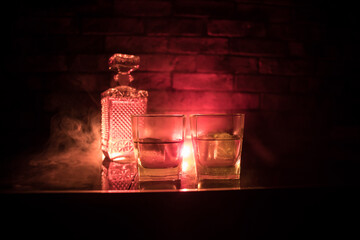 Whiskey in fire concept. Glass of whiskey and ice on wooden surface with color light and fog on background. Close up. Selective focus