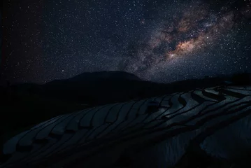Foto op Aluminium Rijstvelden Milky way in the dark night over Pa Bong Piang rice terrace fields and light from countryside village hill of Chiang Mai Thailand.