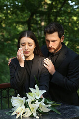 Obraz premium Sad couple mourning near granite tombstone with white lilies at cemetery. Funeral ceremony