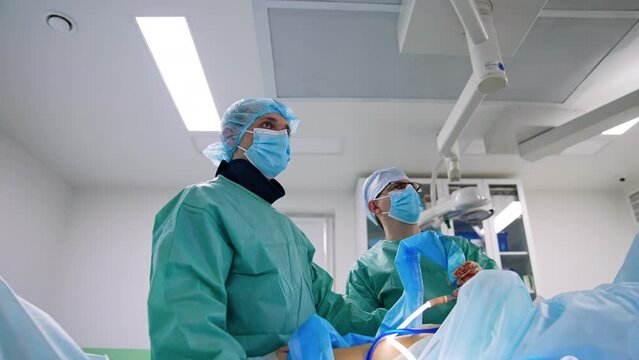 Professional surgeons hold modern surgical devices at operation. Specialists look intently on the monitor in front of them.