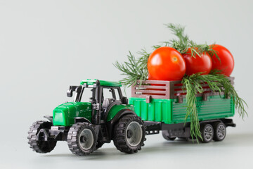 Green toy tractor carries fresh red tomatoes and herbs in a trailer. The concept of agricultural work, harvesting and delivery of crops. Toy world. Photo. Selective focus