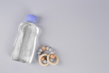 Bottle with baby oil and rattle on light grey background, flat lay. Space for text