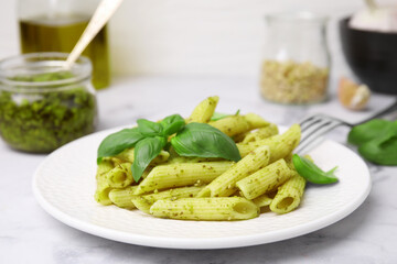 Delicious pasta with pesto sauce and basil on white marble table, closeup