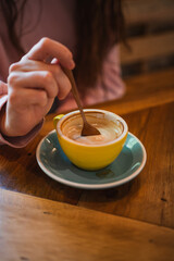Close up of young woman's hand stirring cappuccino coffee cup with spoon in a cafeteria