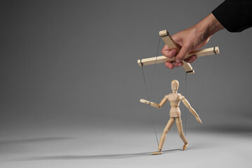 Man pulling strings of puppet on gray background, closeup. Space for text
