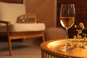 Glass of white wine and flowers on table in room, space for text. Relax at home