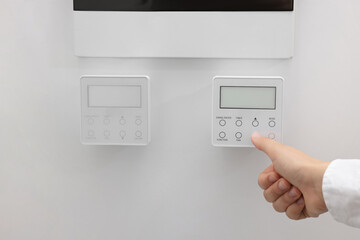 Woman adjusting thermostat on white wall, closeup. Smart home system