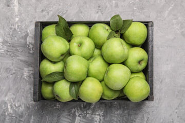 Wooden crate with fresh green apples on grey textured table, top view