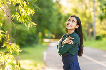 Happy young Asian woman relaxing outdoors, Enjoy beauty of nature and find inner peace on a sunny afternoon, relax time, love your self. Hugging.