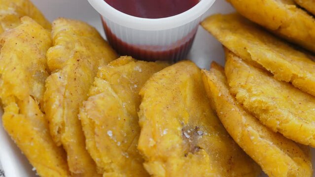 Fried platanos and sauce on plate. Sliced and cooked tostones. Rotating