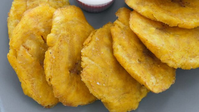 Fried platanos and sauce on plate. Sliced and cooked tostones. Rotating