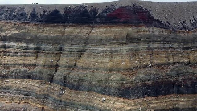 Pan across sedimentary rock strata on steep wall in volcano crater