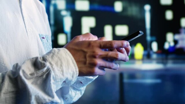 Close up shot of aimless man strolling around city streets at night, chatting with his buddies using smartphone in urban setting. Carefree person enjoying empty town with no cars, using mobile phone