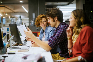 Young group of coworkers going over paperwork in the office of a startup company