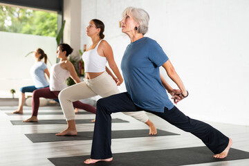 Active woman with group of adult people doing stretching workout for body flexibility in yoga studio