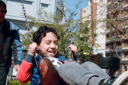 Latino single father playing with his son on swing in public park, copy space