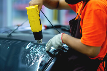 Technician uses equipment to install car window film. - obrazy, fototapety, plakaty