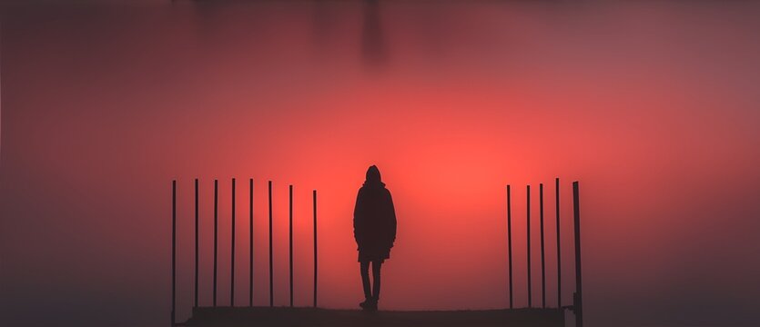 Silhouette of a person standing on the side of a wooden fence on a foggy night with red sky from Generative AI