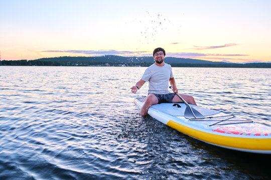 A man sits on a paddle board at sunset.
