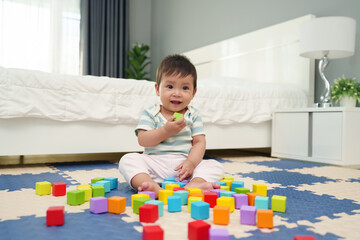 happy infant baby playing wooden block toy on jigsaw mat in bedroom