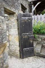 Heavy wooden door set in thick stone masonry wall with stone stairs and picket fence visible behind