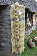 Heavy braid of handspun wool yarn and handwoven shawl dyed with natural plant colors hanging outside a rustic thatched-roofed cottage
