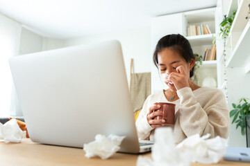 Chinese woman feel sick working from home office. Asian female blowing nose with tissue holding cup of herbal tea. - obrazy, fototapety, plakaty