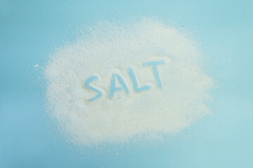 the word salt is written with salt on a blue table. Salt grain top view on blue background.