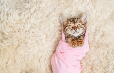 Tiny newborn bengal kitten wrapped like a baby sleeps on a fur bed. Top down view. Empty space for...