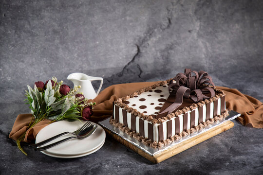 Square Chocolate Cake with rose flowers, spoon and fork served on board isolated on napkin side view of cafe baked food