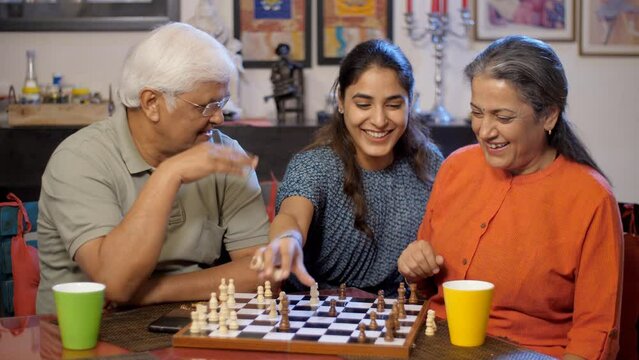 An elderly couple and their granddaughter are playing a game of chess together - joint family  happy family  Asian people. A young girl is having a good time with her grandparents - two generations...