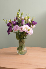 Bouquet of eustomas on a round wooden table on green background. Home interior.