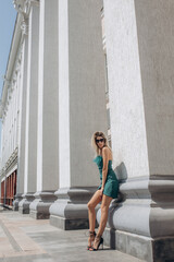 Beautiful blonde model, fashionable in an evening short dress, poses against the background of the columns of the building