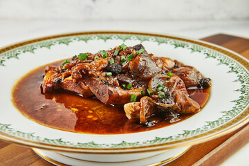 Ossobuco with garlic and green onions in red wine on plate with an ornament