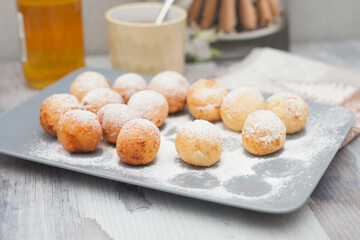 Curd donuts in powdered sugar on a plate, round donuts with a cup of tea