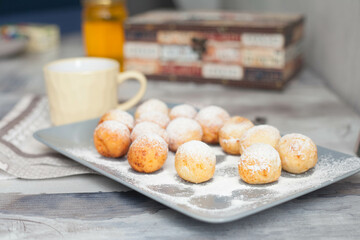 Curd donuts in powdered sugar on a plate, round donuts with a cup of tea