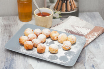 Curd donuts in powdered sugar on a plate, round donuts with a cup of tea