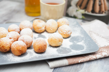 Curd donuts in powdered sugar on a plate, round donuts with a cup of tea