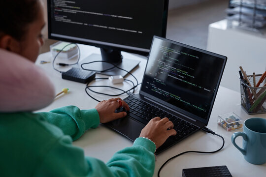 Programmer sitting at her workplace with computers and writing codes on laptop in office