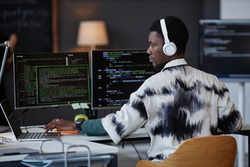 Young African American programmer in wireless headphones working with security codes at his workplace in IT office - obrazy, fototapety, plakaty