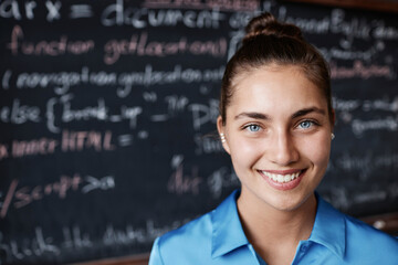 Portrait of smiling young girl looking at camera while standing in the classroom against the blackboard - obrazy, fototapety, plakaty