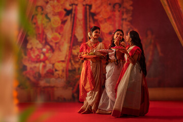 Mother and daughters standing with puja thali during Durga Puja celebration