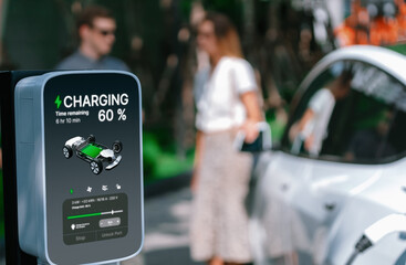 Young couple travel with EV electric car charging in green sustainable city outdoor garden in summer shows urban sustainability lifestyle by green clean rechargeable energy of electric vehicle innards