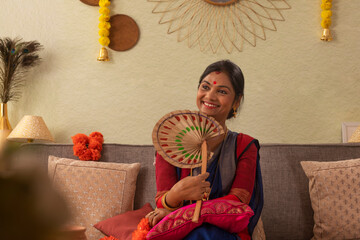 Portrait of cheerful Bengali married woman relaxing on sofa with hand fan