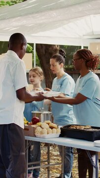 Vertical video People from many backgrounds assemble outside to distribute non-perishable donations and help the poor and homeless. Multiracial volunteers provide needy individuals with free, freshly