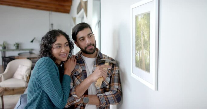Happy biracial couple looking at painting on wall at home, in slow motion