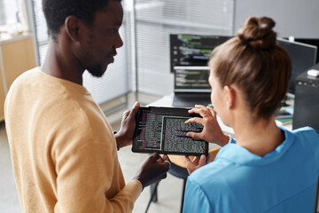 Rear view of young colleagues discussing codes of software on digital tablet together in office