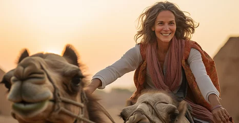 Rolgordijnen A mature woman with gray hair rides a camel in the desert. © Татьяна Оракова